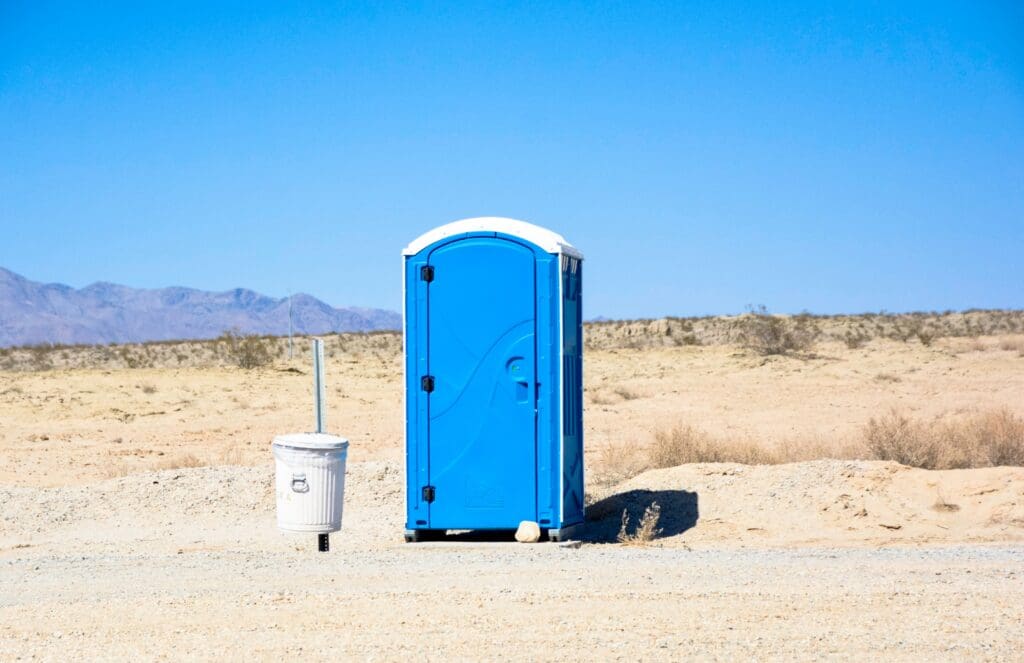A blue porta potty stands alone in the middle of a desolate desert landscape.