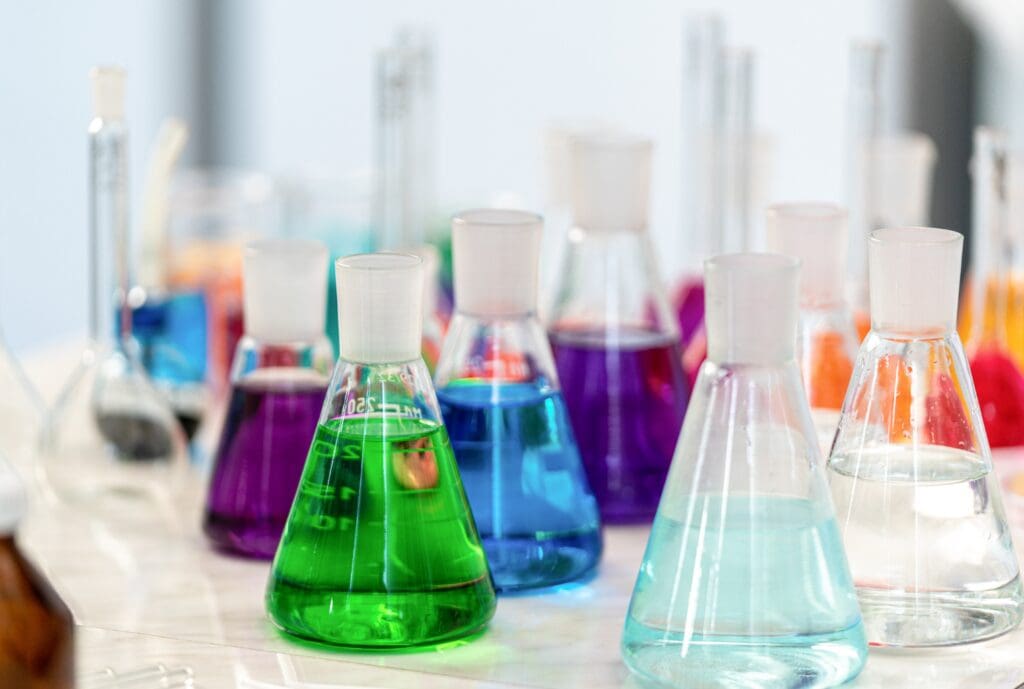 Laboratory flasks filled with colorful chemicals, including green, blue, purple, and clear liquids.