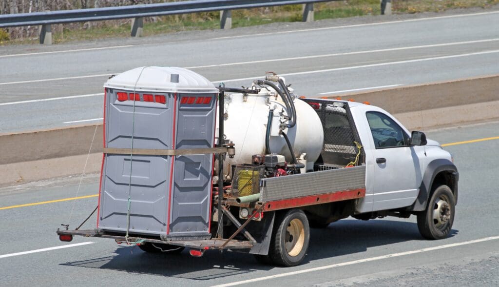 A truck transporting a portable toilet and sanitation equipment on a highway.