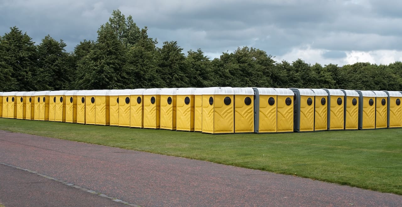 Long Row Of Yellow Portable Chemical Toilets Set Up For A Music Festival Under A Cloudy Sky
