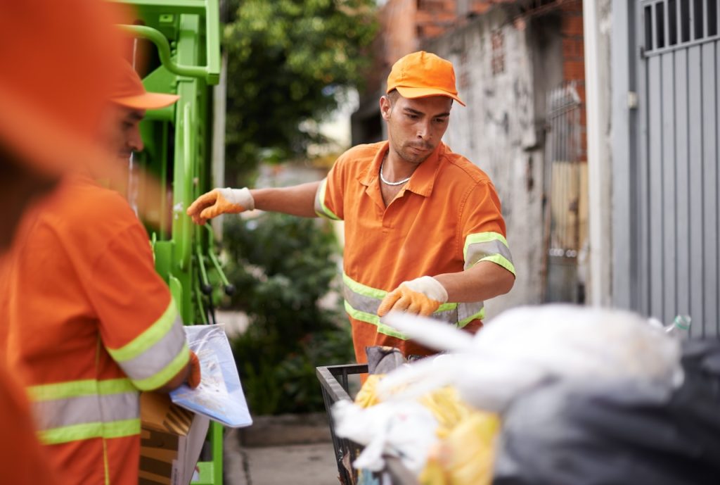 Men, garbage truck and junk collection service on street for public environment with teamwork for junk, recycling or waste management. Uniform, maintenance and dirt transportation, sanitation or refuse